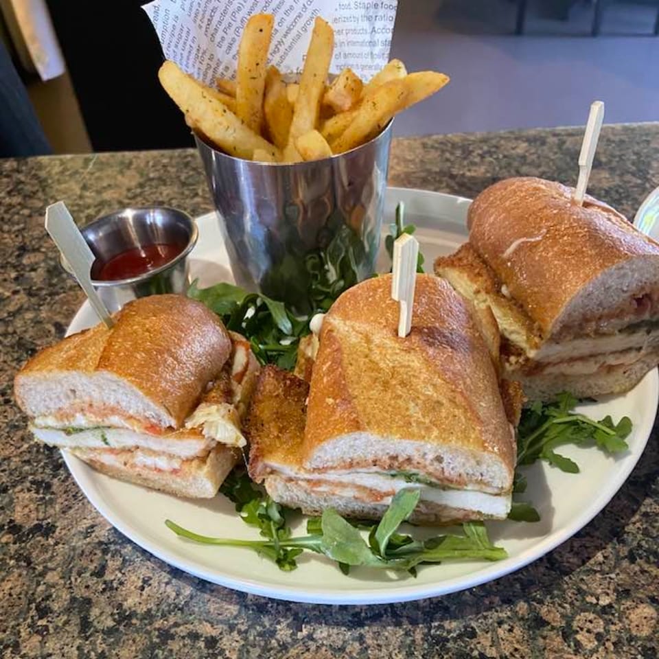 Three chicken parmesan sandwiches on baguettes with a side of fries and ketchup.