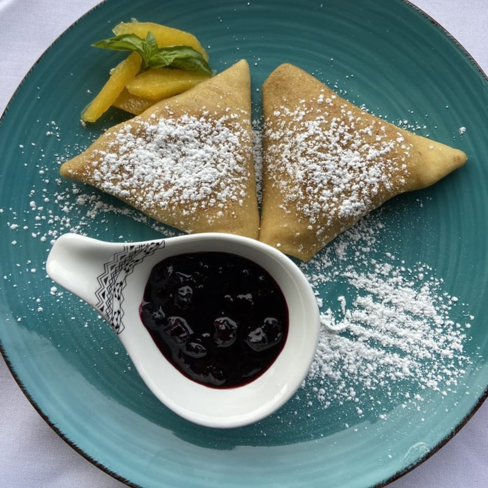 Two powdered sugar crepes with blueberry sauce and orange slices on a teal plate.