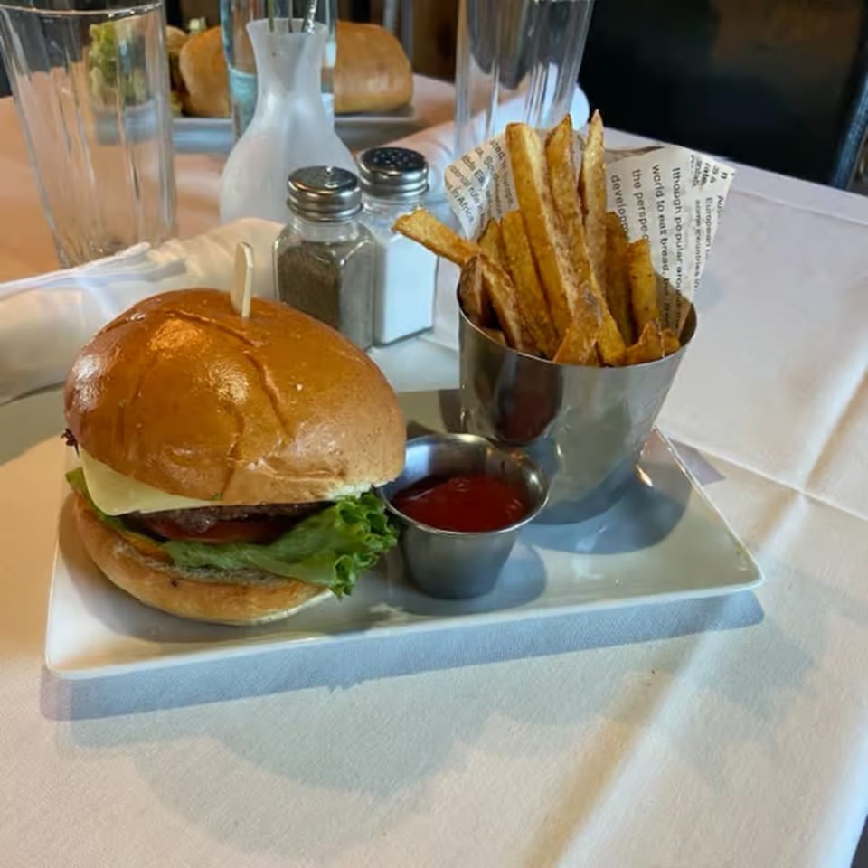 A gourmet burger with cheese, lettuce, and tomato, served with fries and ketchup on a white plate.