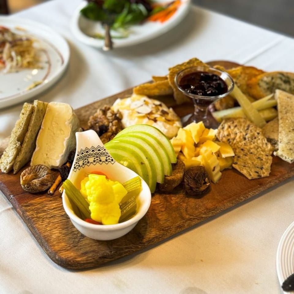 A European charcuterie board with cheeses, crackers, sliced apples, dried figs, nuts, and jam.