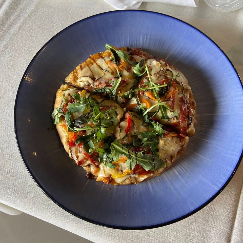 A European flatbread pizza, topped with arugula, bell peppers, and mushrooms, on a blue plate.