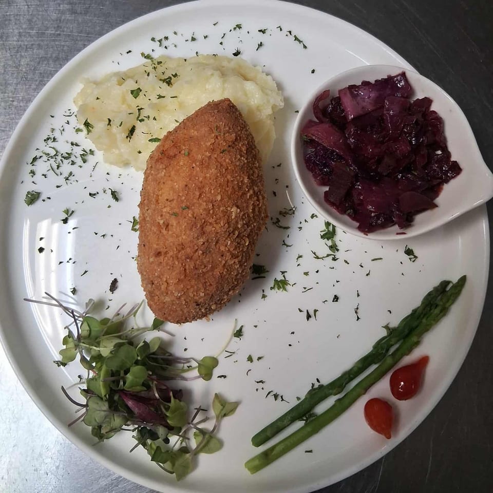 Breaded cutlet with mashed potatoes, red cabbage, asparagus, microgreens, and two small red peppers.