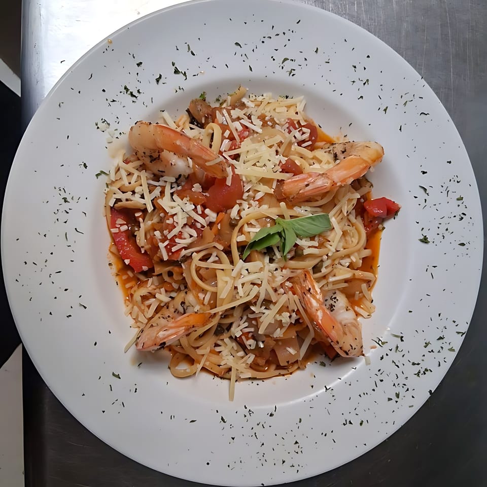 Shrimp linguine pasta with tomato sauce, shredded cheese, and basil on a white plate.