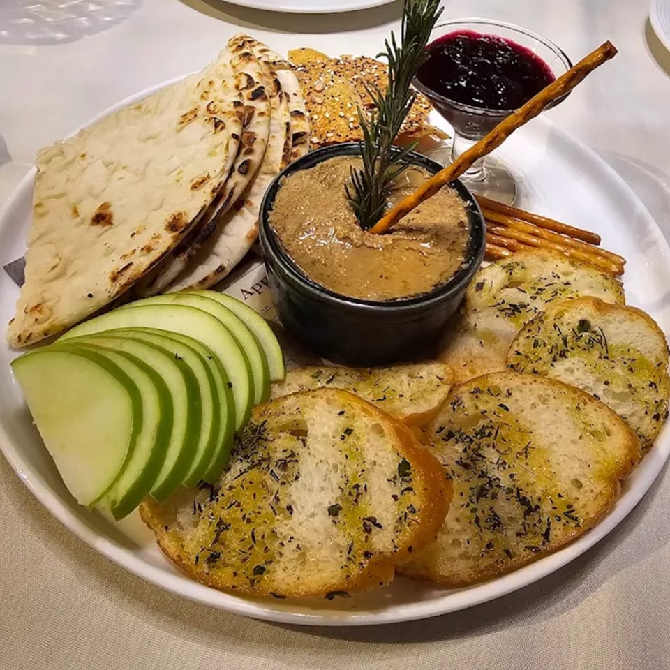 A European appetizer platter with pâté, flatbread, sliced apples, toasted bread, and berry jam.