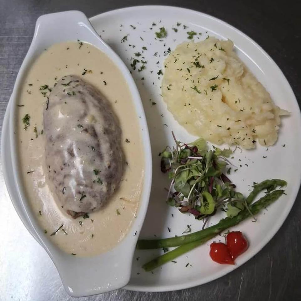 European dish with a meatloaf-like item in cream sauce, mashed potatoes, asparagus, and greens.