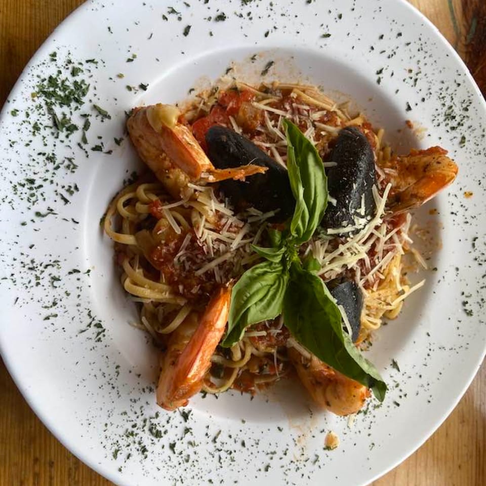 Seafood pasta with shrimp, mussels, tomato sauce, parmesan, and basil on a white plate.